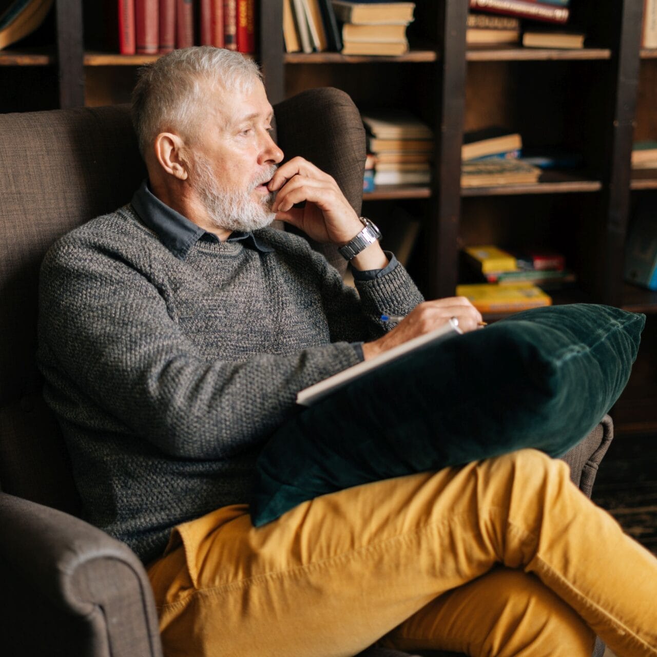 Portrait of sad depressed mature man telling sad story while sitting in comfortable armchair. Bearded gray-haired male talking about his problems to psychologist during psychological consultation.